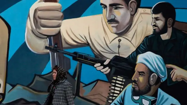 इराणच्या एका भिंतीसमोरून चालणारी महिला 