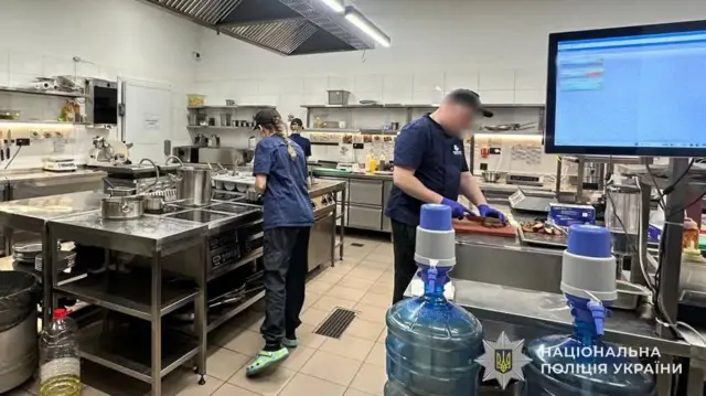 Велика кухня закладу харчування, на ній співробітники у формі із заблюреними обличчями