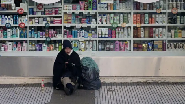 Mulher idosa em situação de rua em frente a farmácia