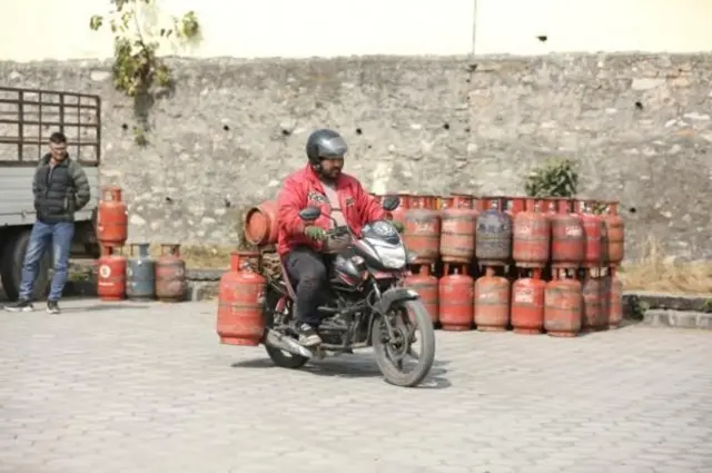 एउटा कालो रङको होन्डा बाइकमा दुइवटा सिलिन्डर बोकेर हिँडेका एक पुरुष। 