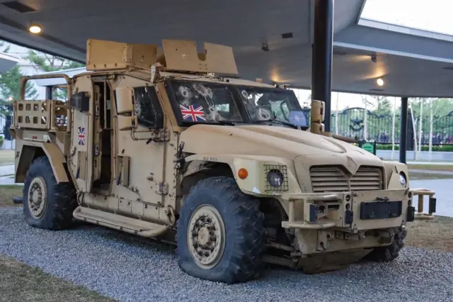 Военный автомобиль с приклеенными британскими флажками и следами от пуль на лобовом стекле.