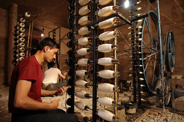 دو مرد رشته‌های ابریشمی را توسط چرخ‌های مخصوص به دور دوک می‌پیچند