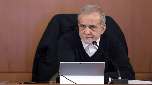 El presidente de Irán, Masoud Pezeshkian, con gesto serio, ante un micrófono en una mesa