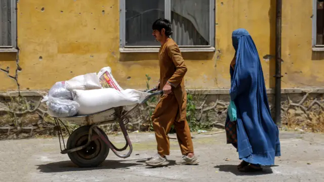 تصویر یک زن و یک مرد که از یکی از مراکز توزیع کمک مقداری کمک دریافته اند. این مرد و زن که ظاهرا مادر و پسر به نظر می‌رسند کمک دریافتی شان را به وسیله یک کراچی انتقال می‌دهند. زن چادری آبی پوشیده و مرد جوان پیراهن محلی زرد رنگ به تن دارد.