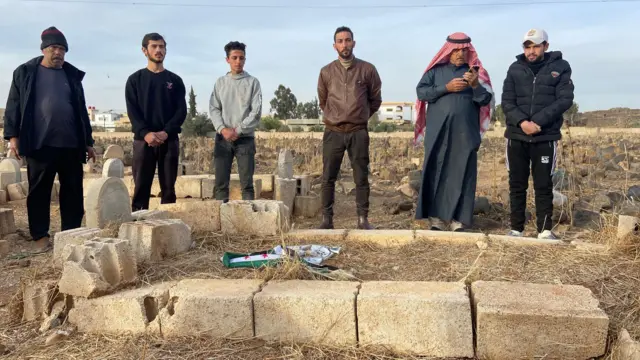 Los vecinos observan en silencio cómo la bandera de la oposición siria es atada alrededor de la lápida de Hamza.