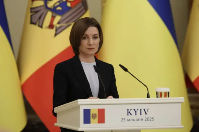Мая Санду під час пресконференції перед стійкою за мікрофоном. На тлі – великі прапори Молдови та України.