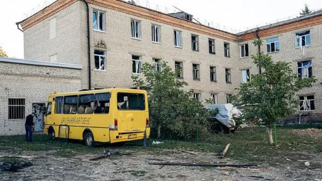 Шкільний жовтий автобус стоїть біля пошкодженої будівлі школи.
