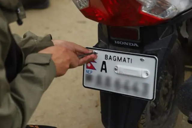 मोटरसाइकलमा इम्बोस्ट प्लेट जडान गर्दै एक मिस्त्री