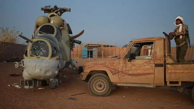 Dis Azawad Liberation Front (FLA) soldier stand on pick-up truck next to damaged Mi-24 helicopter, for di former Africa Corps barracks for Camp 2 for Kidal on May 6, 2026.
