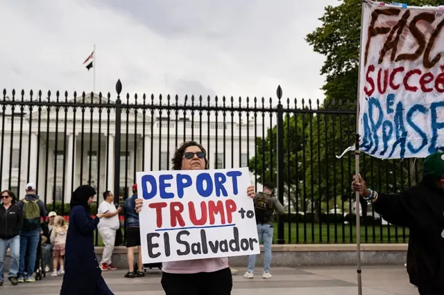 Umugore ufite icyapa cyanditseho ngo "Irukana Trump umujyane muri El Salvador". Uyu mugore ahagaze imbere ya White House