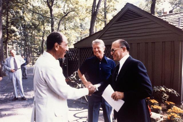 Anwar Sadat e Menachem Begin apertando as mos, com Jimmy Carter ao fundo 