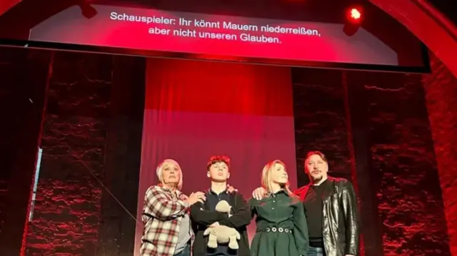 Четверо актеров стоят на сцене в красном освещении с