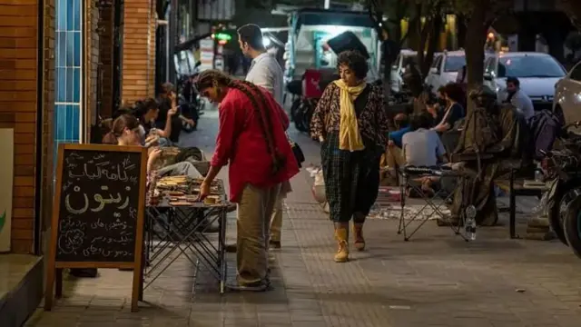 شب هنگام خیابانی در تهران و یک کافه کتاب و چند میز بیرون کافه ودخترانی بدون حجاب