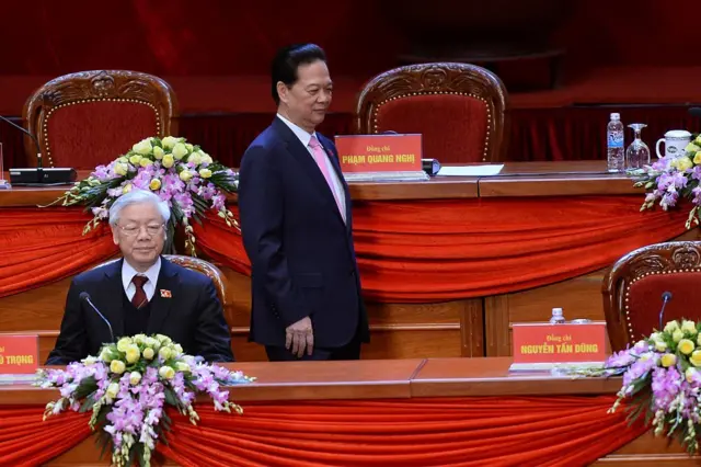 Thủ tướng Nguyễn Tấn Dũng (phải) trở về chỗ ngồi sau khi bỏ phiếu, trong khi Tổng Bí thư Nguyễn Phú Trọng ngồi trên bục phát biểu trong lễ bầu các thành viên Ban Chấp hành Trung ương mới vào ngày thứ sáu của Đại hội Đảng 12, ngày 26/1/2016