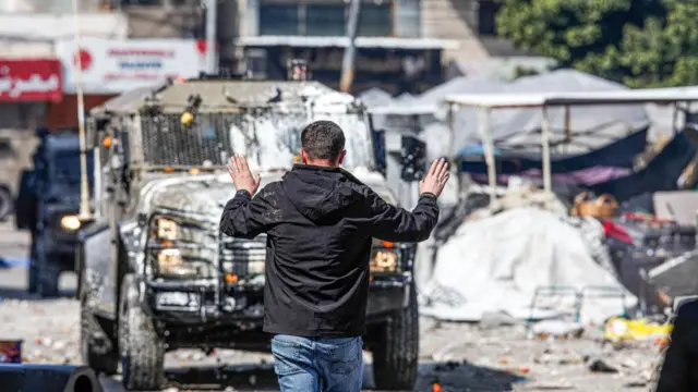 ইসরায়েলি বাহিনীর গাড়ির সামনে হাত উঁচিয়ে এক ফিলিস্তিনি যুবক