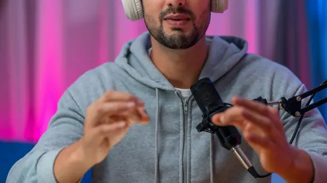 Un joven con sudadera gris, hablando al micrófono en un estudio de podcast profesional centrado en el crecimiento, la estrategia y la inspiración