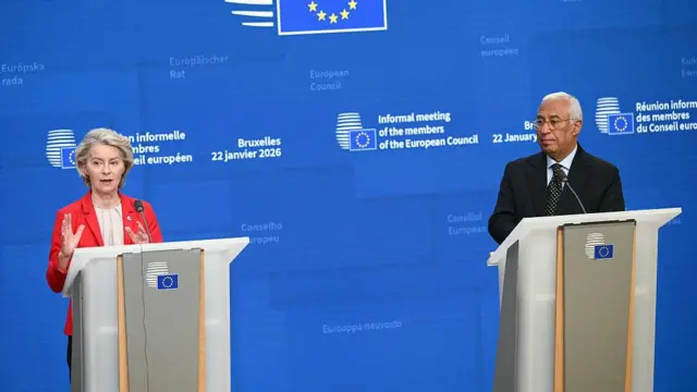 Kırmızı formal kıyafetli bir kadınla, yanındaki başka bir kürsüde beyaz saçlı bir erkek basın toplantısı yapıyor. Kadın yetkili konuşuyor.