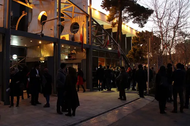 چندین نفر بیرون یک سالن کنسرت ایستاده‌اند