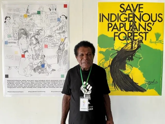 Seorang papua sedang berdiri di depan poster save indigigenous Papuan Forest