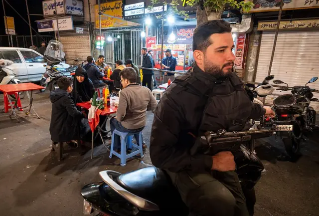 یک نیروی بسیجی با تفنگ و خانواده در خیابان