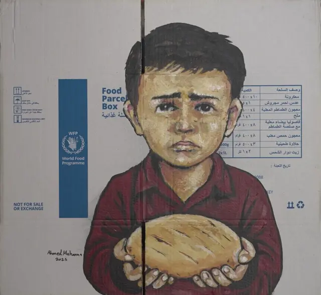 رسم لطفل يرتدي قميصاً خمري اللون وجهه عابس ويحمل بكلتا يديه كسرة خبز على لوحة رسمت من كرتونة مساعدات يظهر عليها شعار برنامج الأغذية العالمي. وباللغة الإنجليزية كتب على كرتونة المساعدات باللون الأزرق وباللغة الإنجليزية "ليس للبيع أو للبدل".