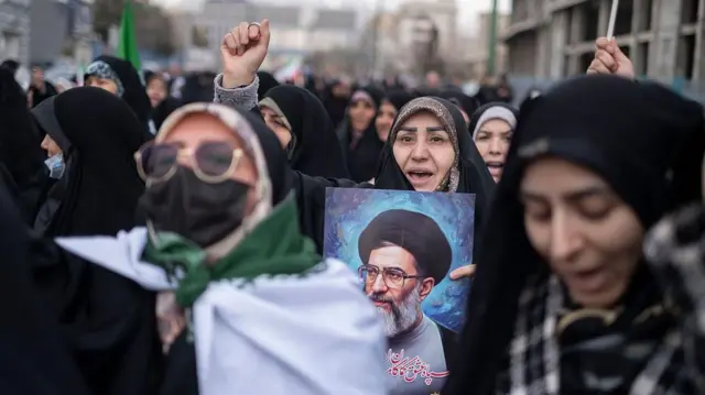 एक बुर्क़ा पहने ईरानी महिला, फ़रवरी 11, 2026 को तेहरान, ईरान में इस्लामी क्रांति की जीत की 47वीं वर्षगांठ के अवसर पर आयोजित रैली के दौरान ईरान के सर्वोच्च नेता, आयतुल्लाह अली खामेनेई का चित्र उठाए हुए, अमेरिका और इज़राइल के खिलाफ नारे लगाती है.