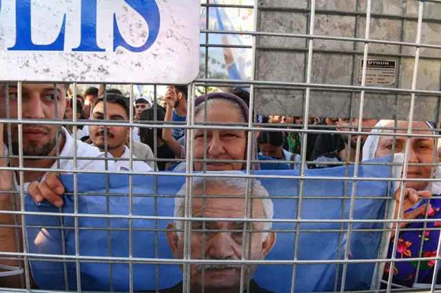 Diyarbakır'daki bir protestoda, başı yarı bağlı bir Kürt kadın, polis bariyerleri arkasından elindeki Öcalan bayrağını açmış. 