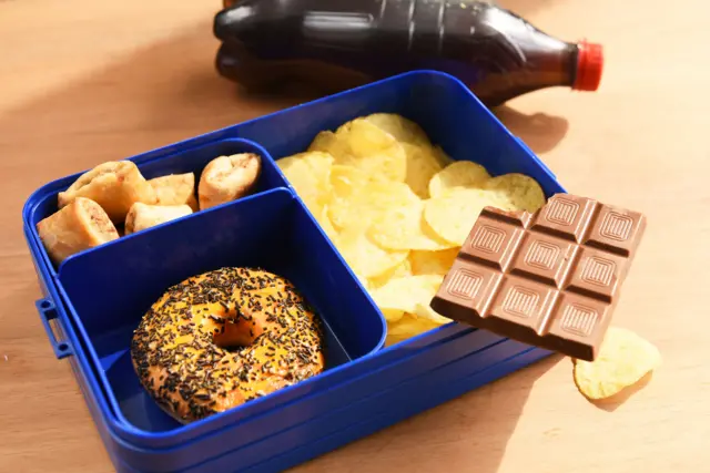 Niezdrowy zestaw śniadaniowy do szkoły - czekolada, cola, bajgiel i chipsy.