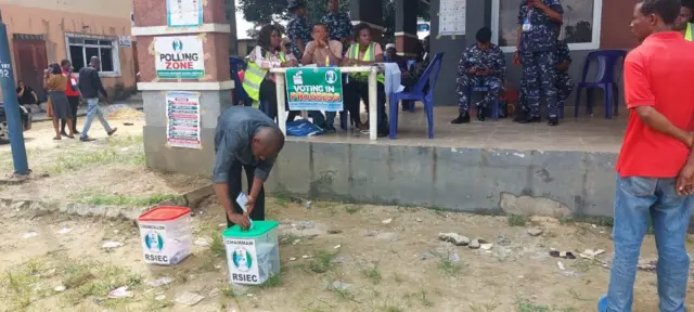 Voter dey cast im vote for Rumuwoji playfield for Ojukwu Diobu, Mile One, Port Harcourt with security Pipo and RSIEC election officials for di background.
