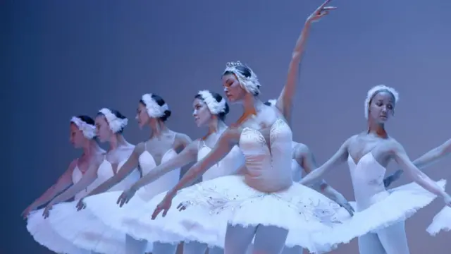 Балерины танцуют в пачках на сером фоне.