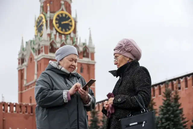 Две пожилые женщины в демисезонных куртках общаются на фоне кремлевской стены