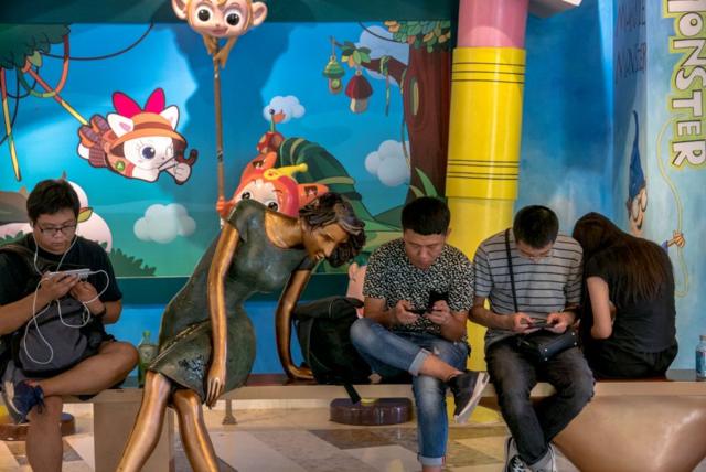 شباب يقرأون ويلعبون على الهواتف المحمولة في أحد مراكز التسوق في الصين.
