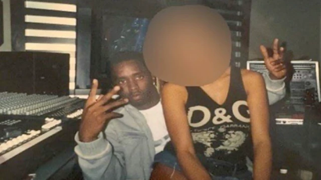 Foto antiga colorida escaneada de um processo judicial, que parece mostrar Sean Combs em seu estúdio, gesticulando com as duas mãos para a câmera, com uma jovem sentada no seu colo. O rosto da mulher está desfocado