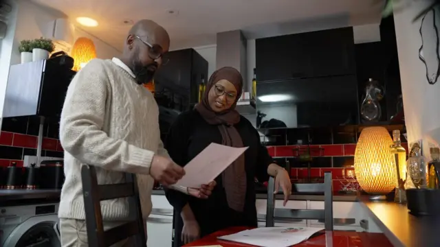 Hana y Fahad miran documentos en su cocina.