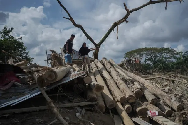 Sekelompok warga melintasi rumah yang rusak pascabanjir di Desa Lintang Bawah dan Desa Sukajadi, Kecamatan Kuala Simpang, Aceh Tamiang.