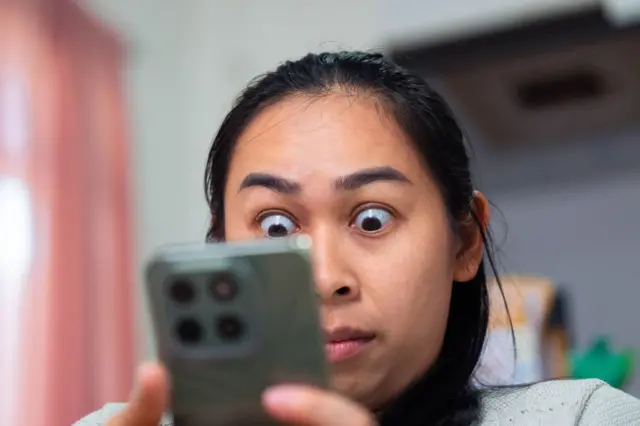 Foto ilustrasi seorang perempuan nampak melotot dan kaget melihat ponselnya.