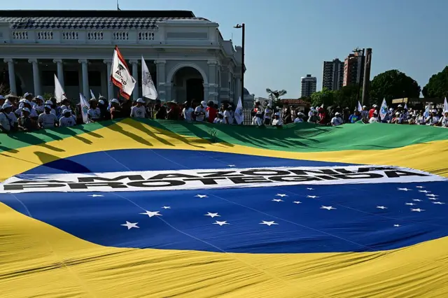 Manifestantes exibem uma enorme bandeira brasileira com os dizeres 'Amazônia Protegida' (em vez de Ordem e Progresso) durante a chamada 'Grande Marcha do Povo' à margem da Conferência das Nações Unidas sobre Mudanças Climáticas COP30, em Belém (PA)