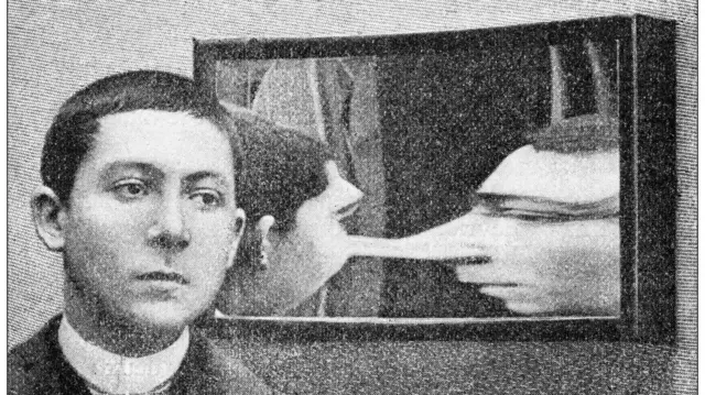 صورة قديمة بالأبيض والأسود لرجل يقف أمام مرآة خداع بصري تشوه ملامح وجهه.