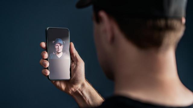 Homem de costas com celular registrando rosto