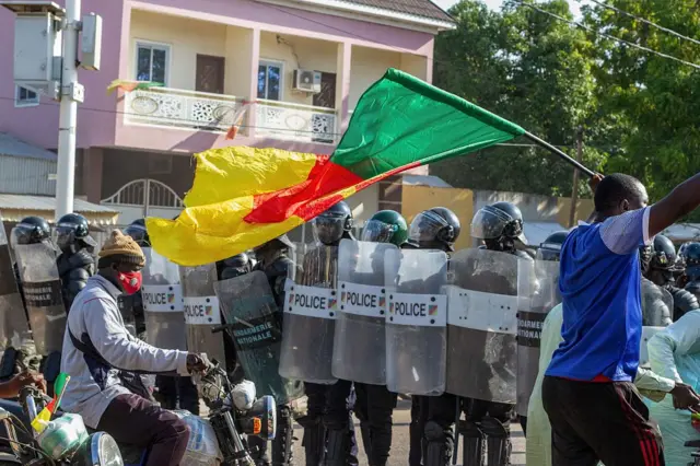 Un homme fait flotter le drapeau camerounais devant des forces de l'ordre avec leur équipent anti émeute