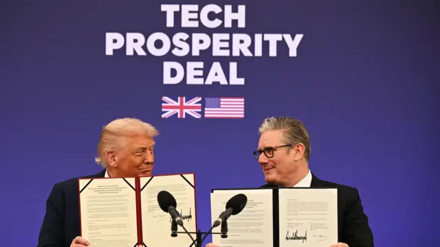Дональд Трамп и Кир Стармер держат в руках подписанный документ (у каждого своя копия) и с улыбкой смотрят друг на друга. За ними надпись Tech prosperity deal, под ней изображены флаги Великобритании и США.