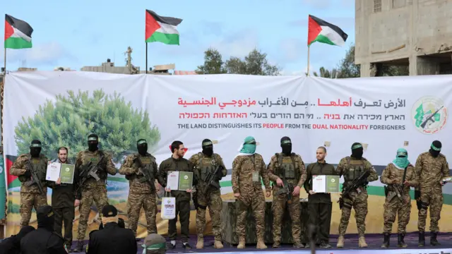 Israeli hostages Omer Shem Tov (2nd Left), Eliya Cohen (5th Left) and Omer Wenkert (4th Right) stand on a stage next to armed Palestinian fighters during a handover ceremony as part of a ceasefire and hostage release deal, in Nuseirat, central Gaza (22 February 2025)