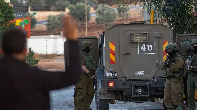 صورة تُظهر جنوداً إسرائيليين يرفعون سلاحهم باتجاه فلسطيني يرفع يديه في الضفة الغربية