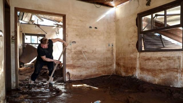 Mulher usa enxada para tirar lama de dentro de casa