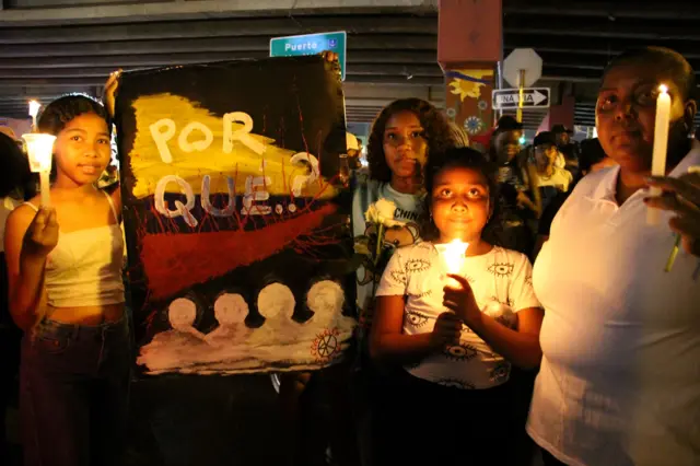 Varias mujeres y niñas portan velas y un cartel.