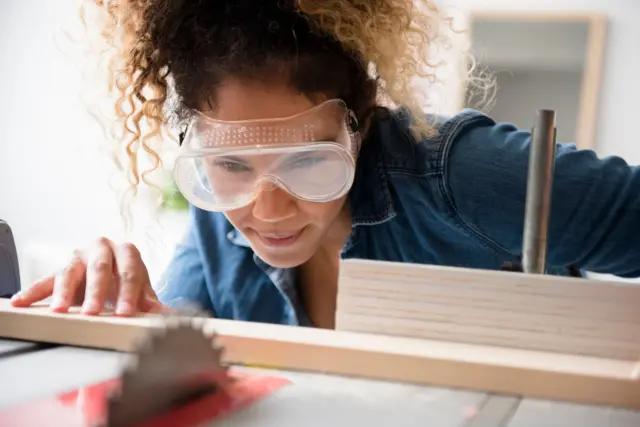 A woman with protective goggle cutting wood with a saw