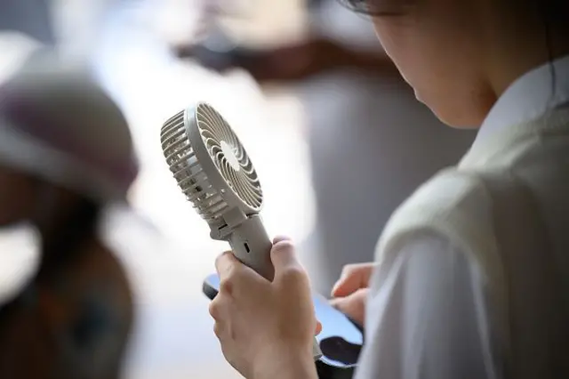 Uma mulher segura um ventilador portátil nas mãos