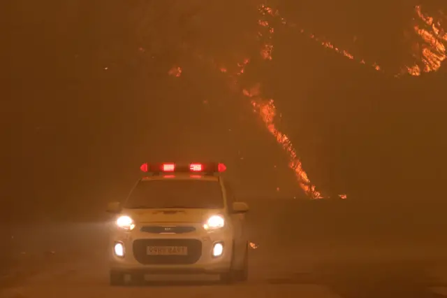 25일 오후 경북 안동시 길안면 백자리에 강풍이 불어 주변 산이 화염에 휩싸인 가운데 소방관계자들이 대피 명령이 내려진 마을 곳곳을 순찰하고 있다