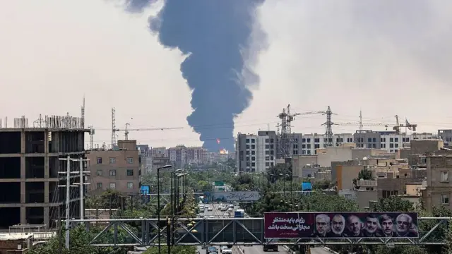 تصاویر ژنرال‌های نظامی و دانشمندان هسته‌ای ایران که در حمله ۱۳ ژوئن اسرائیل کشته شدند، در بالای یک جاده به نمایش گذاشته شده است، در حالی که ستونی از دود و آتش سنگین بر فراز پالایشگاه نفت در جنوب تهران، پس از حمله شبانه اسرائیل در ۱۵ ژوئن ۲۰۲۵، به هوا برخاسته است. تلویزیون دولتی اوایل روز ۱۵ ژوئن اعلام کرد که ایران رگبار جدیدی از موشک‌ها را به سمت اسرائیل شلیک کرده است، در حالی که دو طرف برای سومین روز متوالی به تبادل آتش پرداختند.