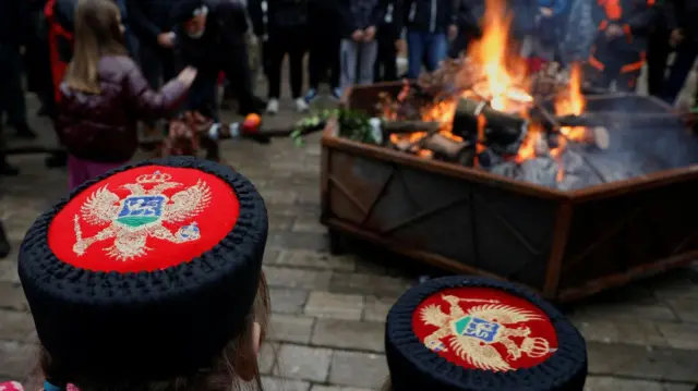 Капе са традиционалним симболима Црне Горе у даљини гори бадњак